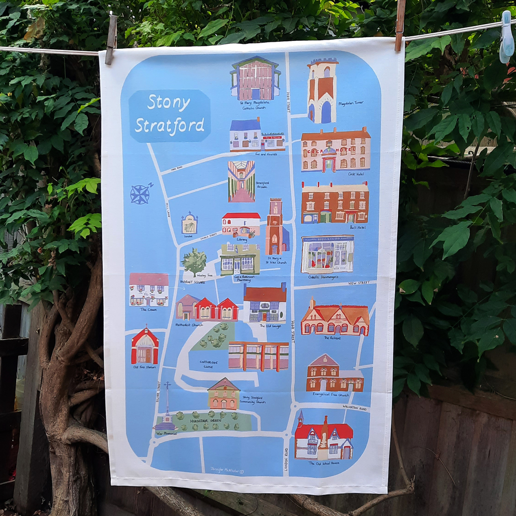 Blue Stony Stratford illustrated cotton tea towel hanging on a washing line outdoors.